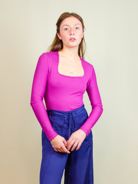 Wearing a long-sleeve bodysuit made from jersey deadstock fabric, featuring a square neckline and a sleek, fitted design. Styled as part of a colorful, slow fashion, made-to-order collection